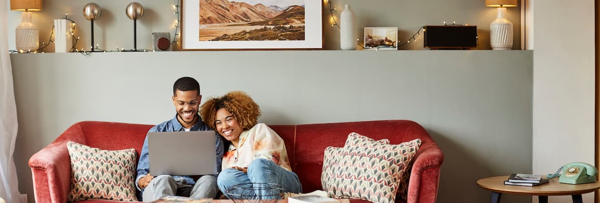 A young couple researches home loans on their laptop sitting on the couch in their living room.
