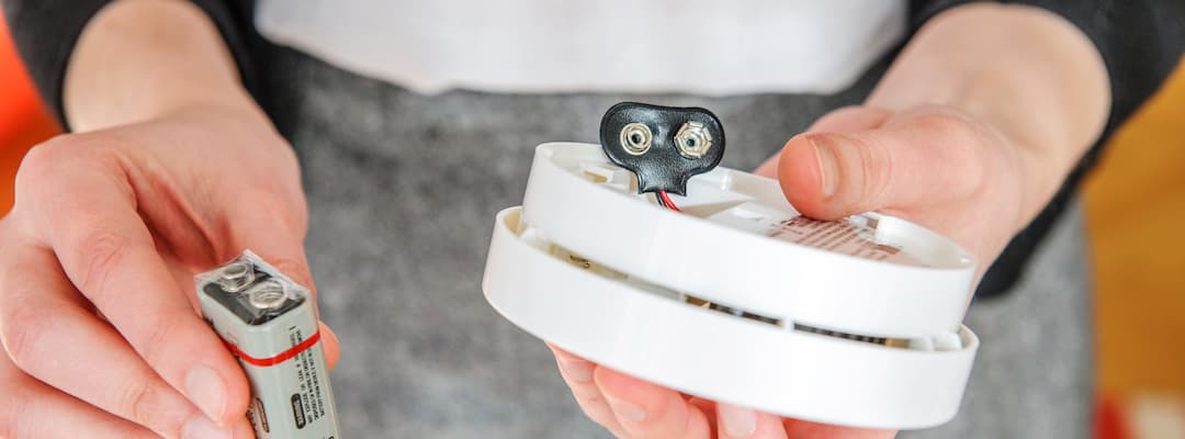 Woman holds a smoke alarm and its batteries