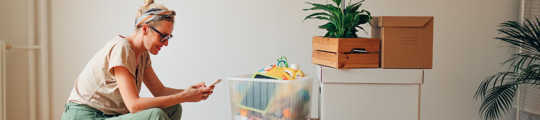 Woman smiles while checking phone in front of boxes to move out of home