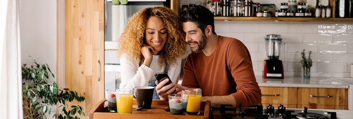 happy couple looking at phone while having breakfast in the kitchen