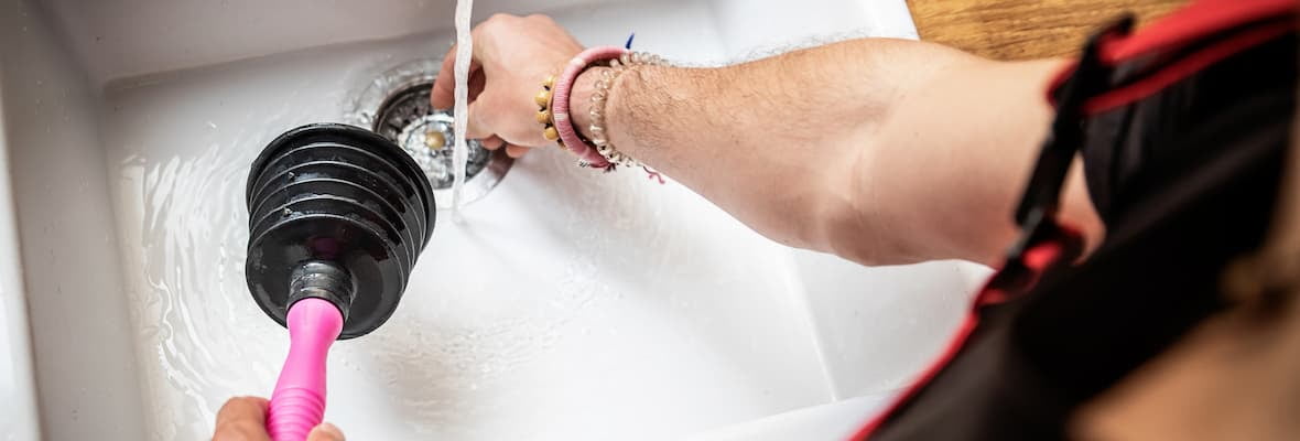 Man unclogging kitchen sink with accordion plunger while water is running.