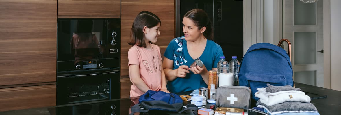 A mother shows her daughter how to prepare an emergency kit inside their modern kitchen.
