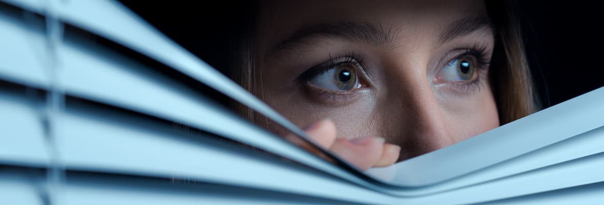 Scared woman peaks out of the blinds at her home