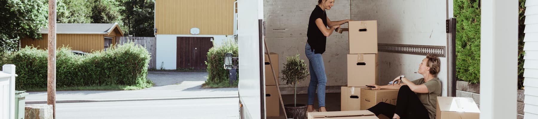 two women packing boxes into moving truck outside of home