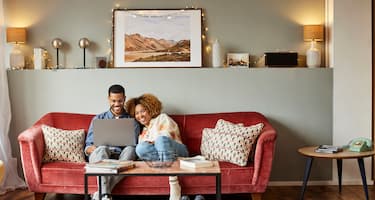 A young couple researches home loans on their laptop sitting on the couch in their living room.
