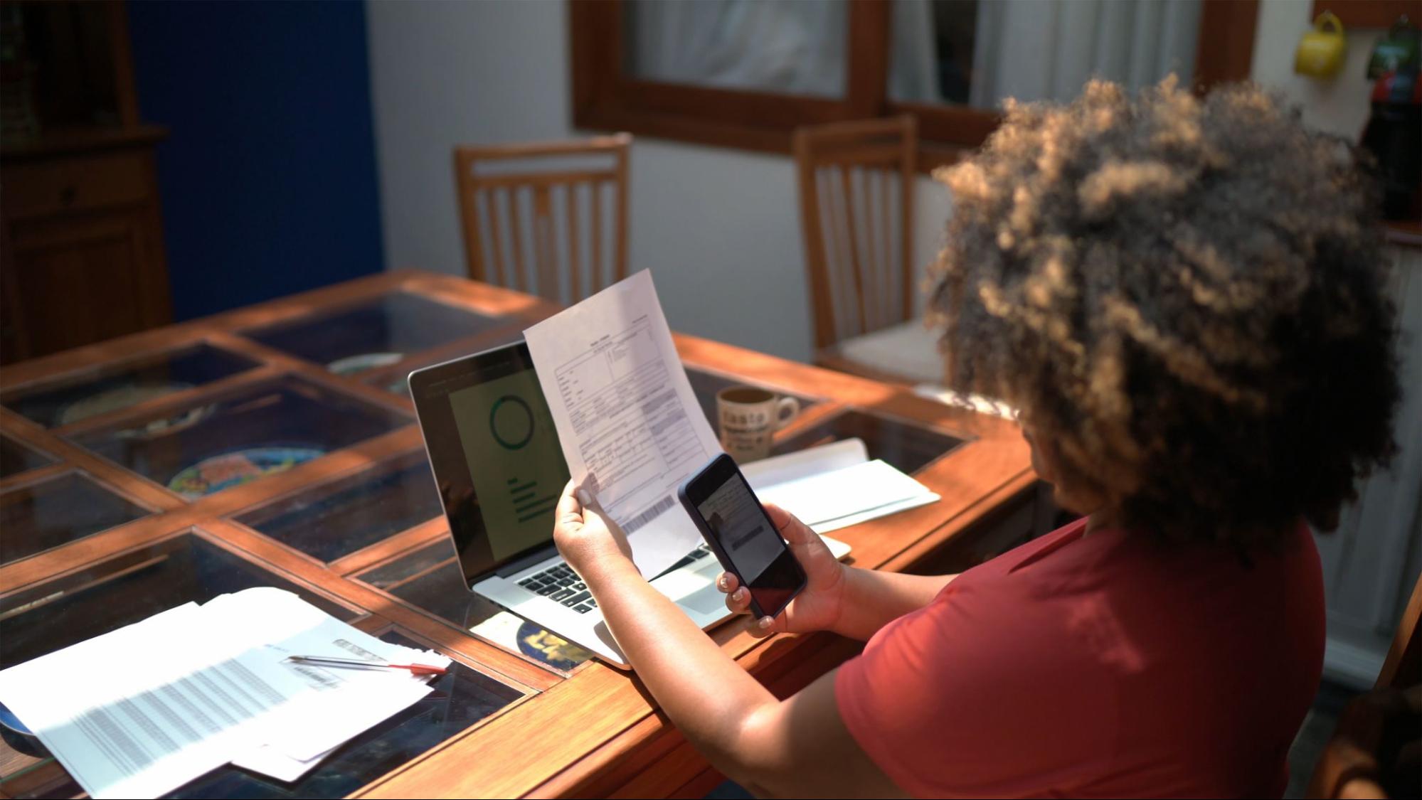 A woman takes a photo of an invoice at a table in her home.