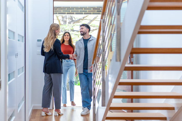 A happy couple is greeted at the door by a real estate agent for a house inspection.