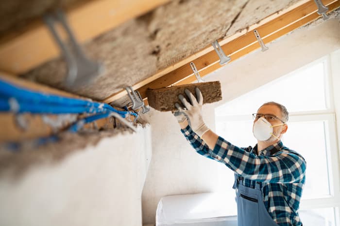 A man installs mineral wool insulation in an attic while wearing a protective mask and gloves.