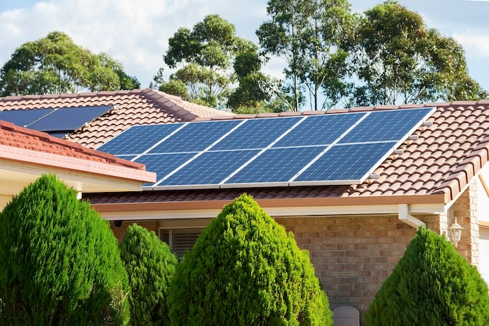 Photovoltaic panels installed on a tiled house roof with trees surrounding the property.