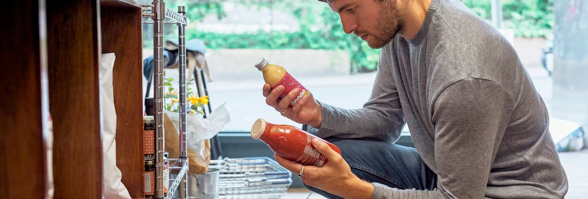 man grocery shopping kneeling down comparing different food products