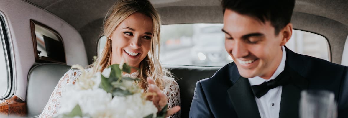 Bride and groom smiling in the backseat of a car