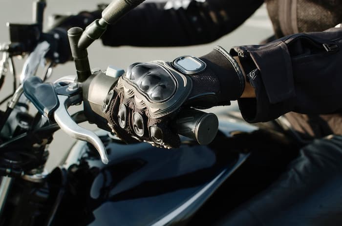 A motorcyclist wears protective gloves while holding the handlebars of their motorcycle.