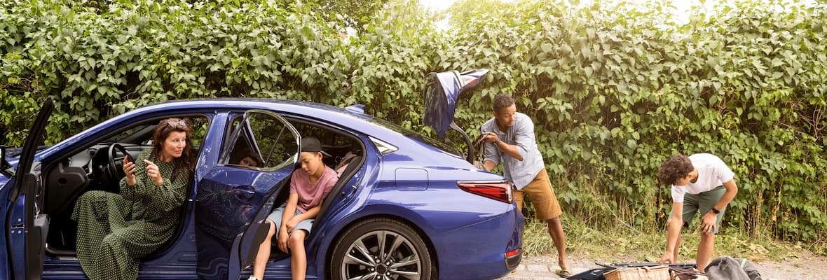 family of four unpacking blue sedan car parked on gravel