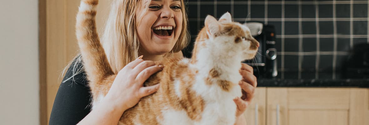 A happy woman pats her ginger and white cat on top of her kitchen counter.