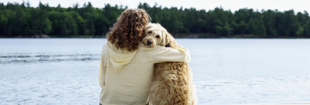 person hugging pet dog on deck in front of lake