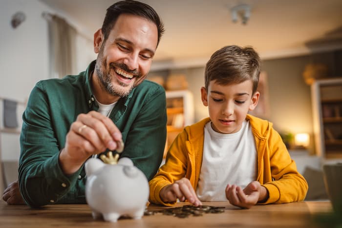 A father and his son count their coins before adding them to a piggy bank.