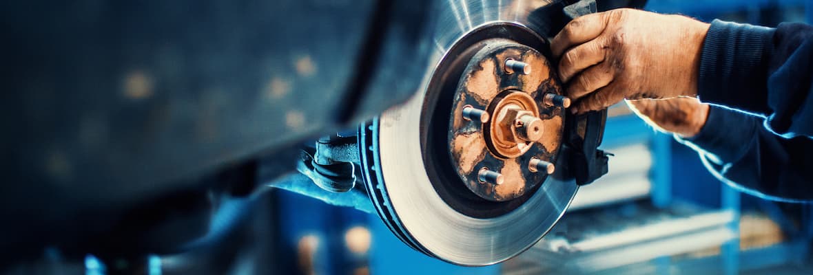 A mechanic replaces car brake pads on a car that was lifted to eye level using a hydraulic jack.