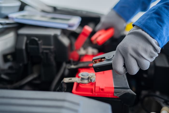 Close up of a gloved hand holding battery charger tools to jump start a car battery