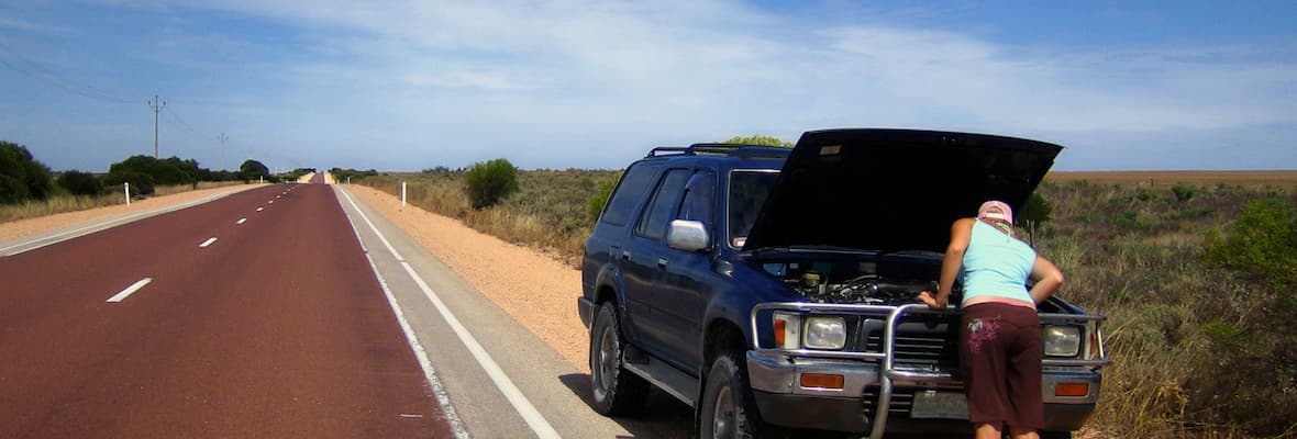 A 4x4 is broken down on the side of an outback road, being checked by the driver