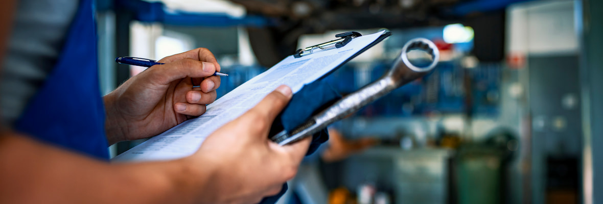 A mechanic holds a car servicing checklist and is marking off work completed