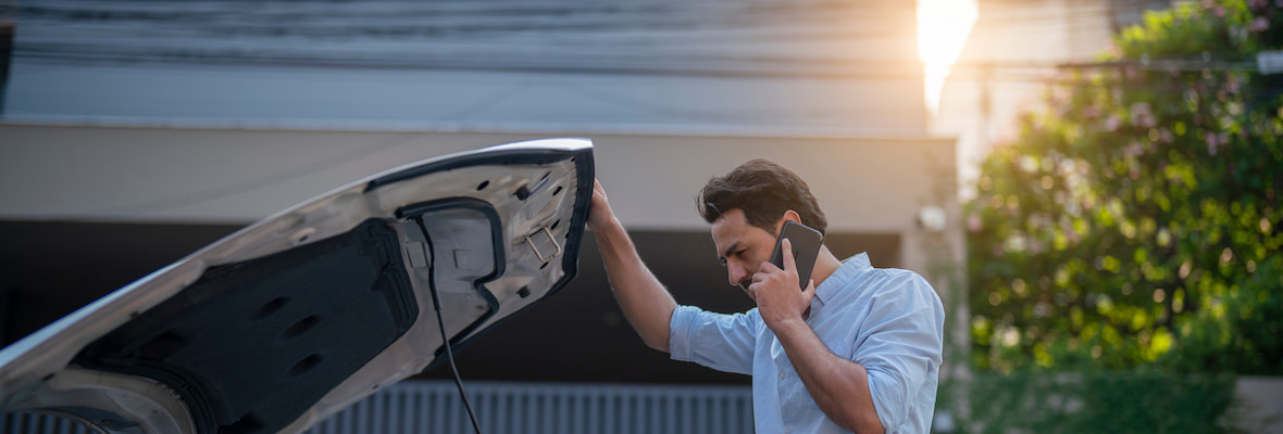 Man looks underneath the bonnet of his car while talking on his mobile phone.