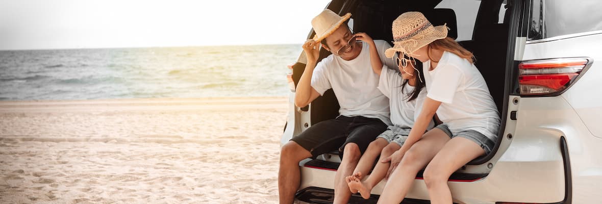 mum dad and daughter sitting in boot of car parked on beach