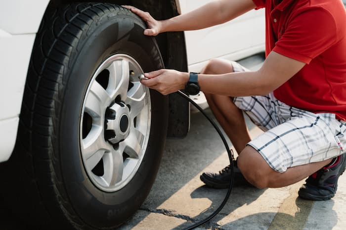 A man crouches down on concrete to connect a tyre inflater to a car tyre.