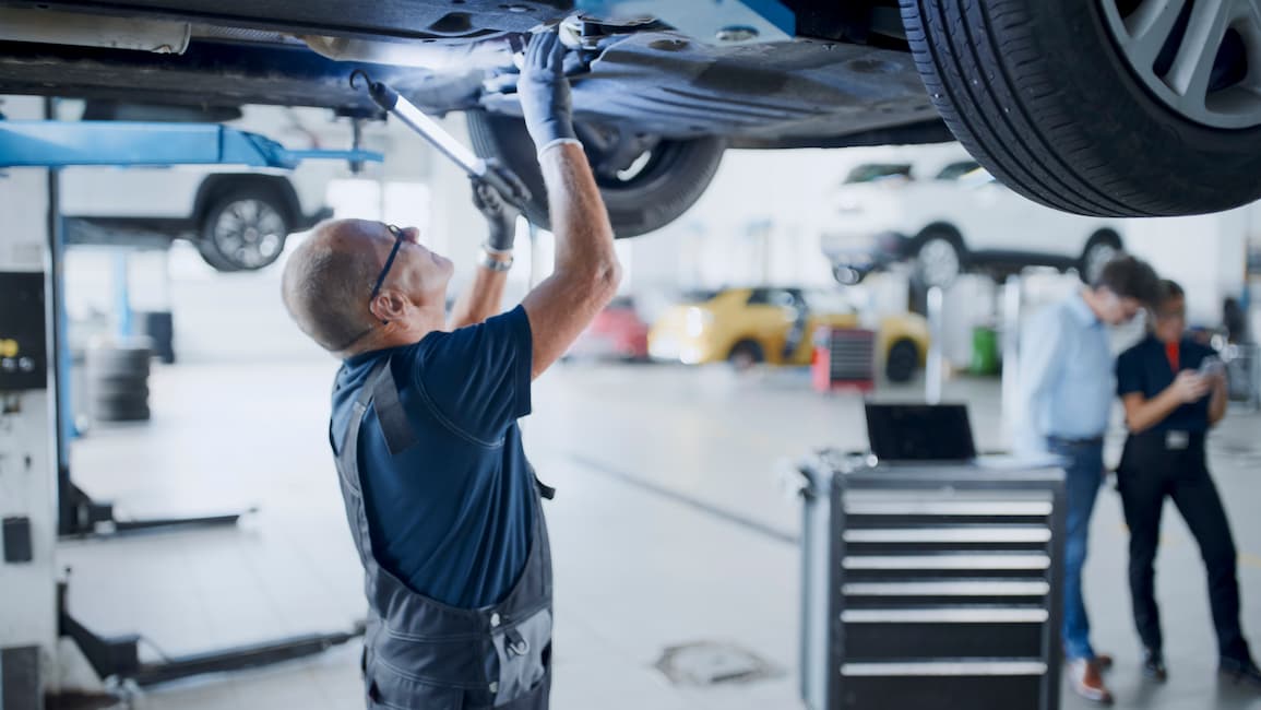 Male mechanic with light working under a car in an auto repair shop