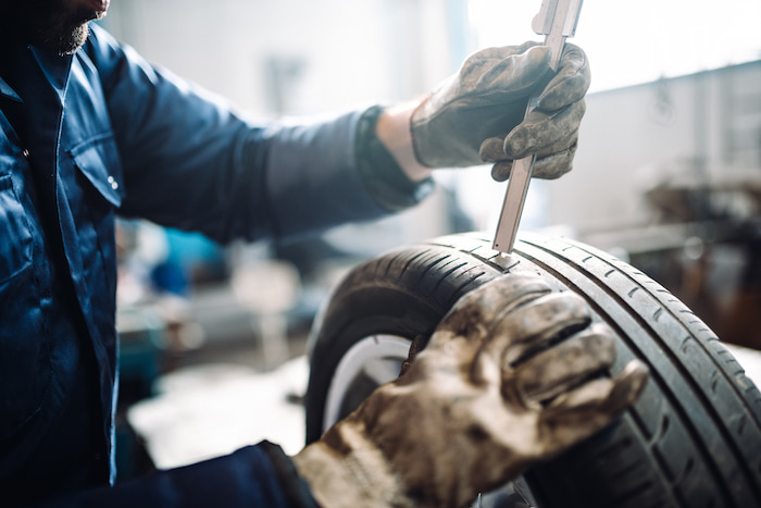 A tyre fitter measures the tread wear using an indicator