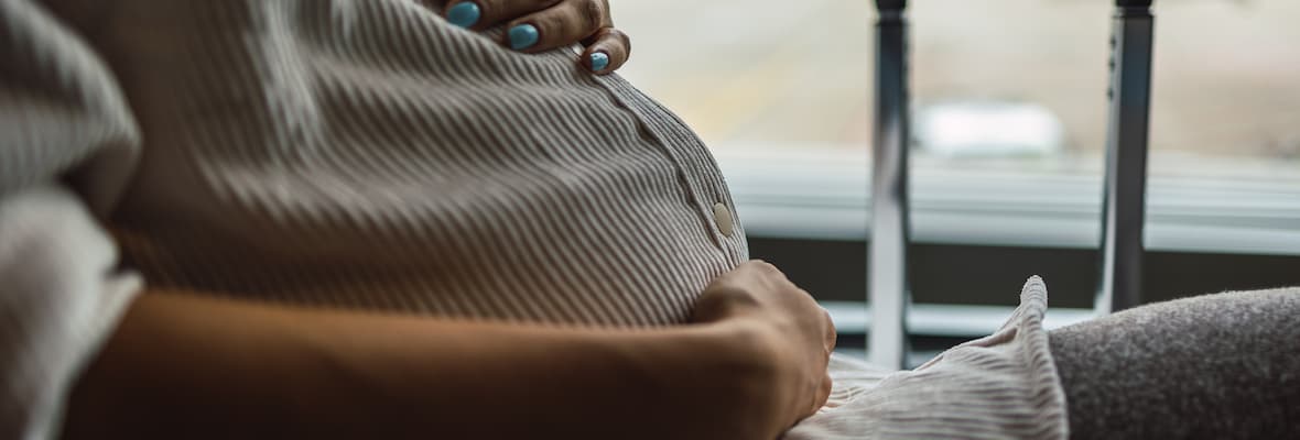 A pregnant woman holds her stomach. She is seated at an airport gate.