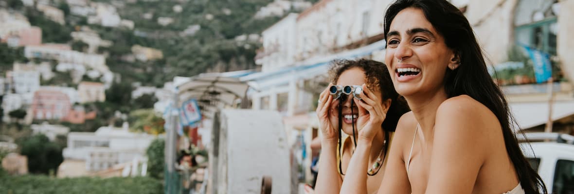 Two young women use binoculars off a balcony in Positano