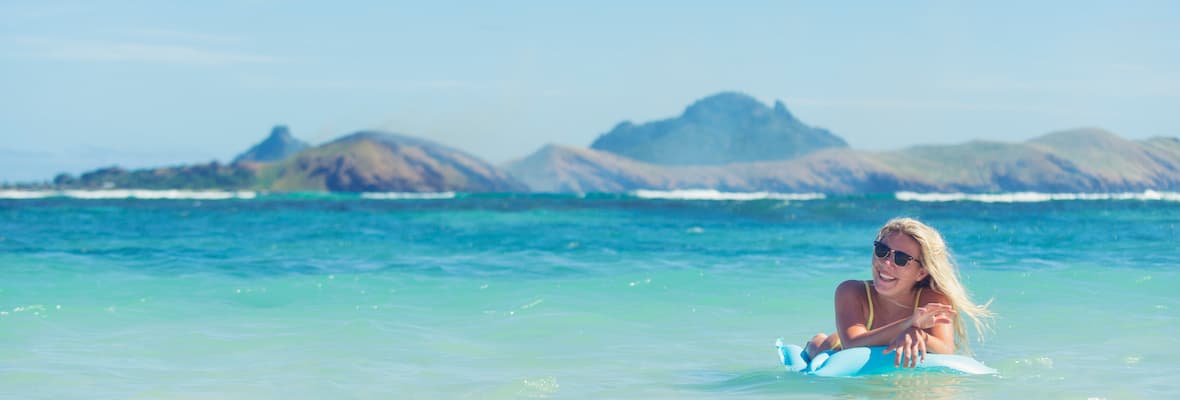 Young woman lies on a pool toy in the ocean on a beach in Fiji
