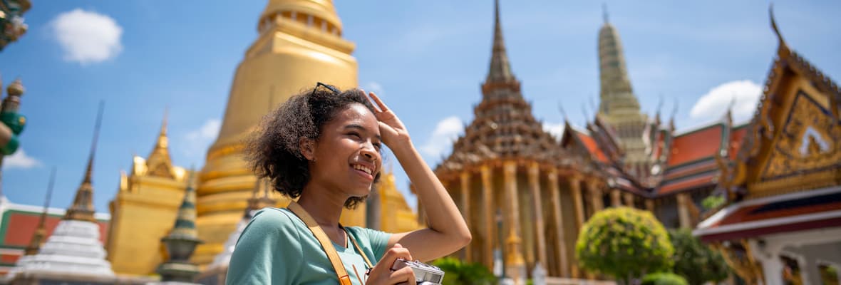 Young woman holds a camera as she walks past the Wat Phra Kaew temple in Bangkok, Thailand. 