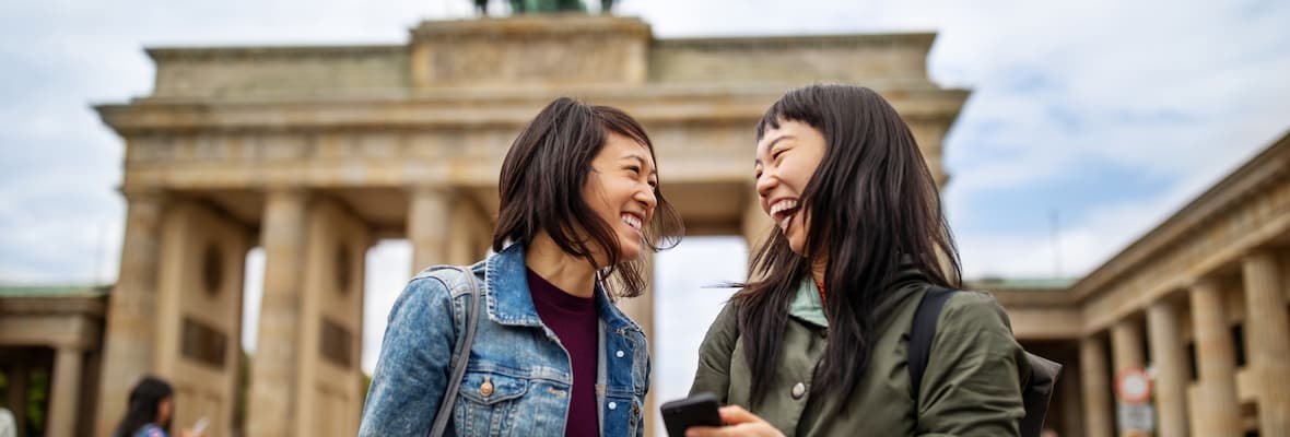 Two friends laugh together in front of the Brandenburg Gate