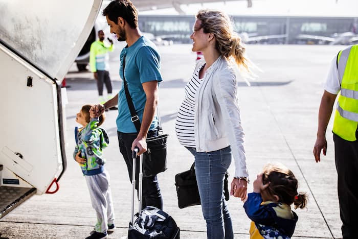 Happy family about to board a flight, including a pregnant mother.