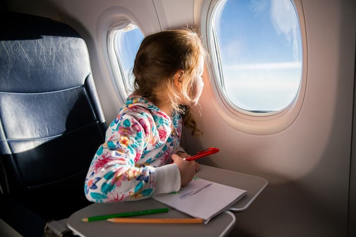 Young girl looks out plane window while colouring