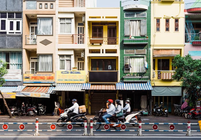 Mopeds speed past colourful buildings on a busy street in Ho Chi Minh City.